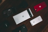 A collection of various smartphones is arranged on a dark surface. The central phone features a distinctive design with a horizontal black band at the top. Surrounding it are other phones, including a red-backed model and a silver-backed one. The layout suggests a comparison or display of different phone models.