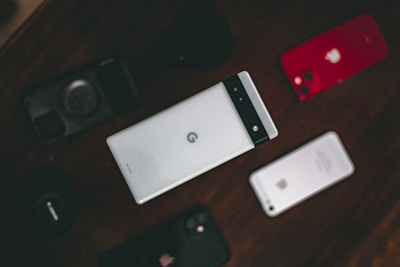 A collection of various smartphones is arranged on a dark surface. The central phone features a distinctive design with a horizontal black band at the top. Surrounding it are other phones, including a red-backed model and a silver-backed one. The layout suggests a comparison or display of different phone models.