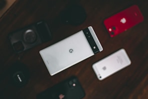 A collection of various smartphones is arranged on a dark surface. The central phone features a distinctive design with a horizontal black band at the top. Surrounding it are other phones, including a red-backed model and a silver-backed one. The layout suggests a comparison or display of different phone models.