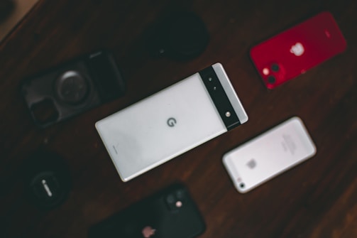 A collection of various smartphones is arranged on a dark surface. The central phone features a distinctive design with a horizontal black band at the top. Surrounding it are other phones, including a red-backed model and a silver-backed one. The layout suggests a comparison or display of different phone models.