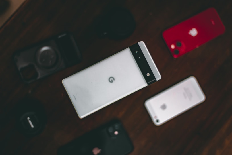 A collection of various smartphones is arranged on a dark surface. The central phone features a distinctive design with a horizontal black band at the top. Surrounding it are other phones, including a red-backed model and a silver-backed one. The layout suggests a comparison or display of different phone models.