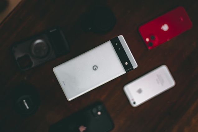 A collection of various smartphones is arranged on a dark surface. The central phone features a distinctive design with a horizontal black band at the top. Surrounding it are other phones, including a red-backed model and a silver-backed one. The layout suggests a comparison or display of different phone models.