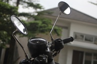 Close-up of a motorcycle handlebar with the mountain vista reflected in the rearview mirror.