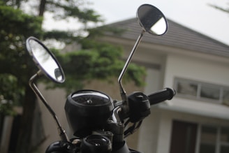 Close-up of a motorcycle handlebar with the mountain vista reflected in the rearview mirror.