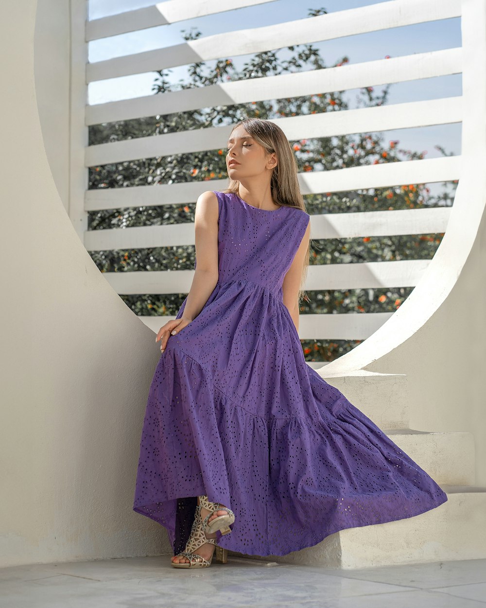 a woman in a purple dress leaning against a wall