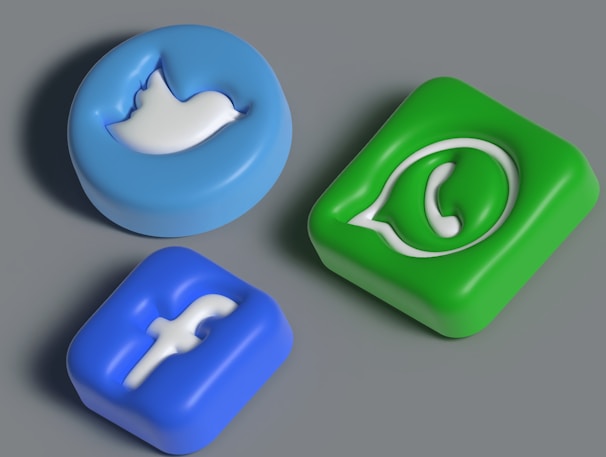 Three three-dimensional icons representing popular social media platforms are arranged against a neutral background. The icons have an embossed look, featuring a blue bird, a blue letter 'f', and a green phone symbol.
