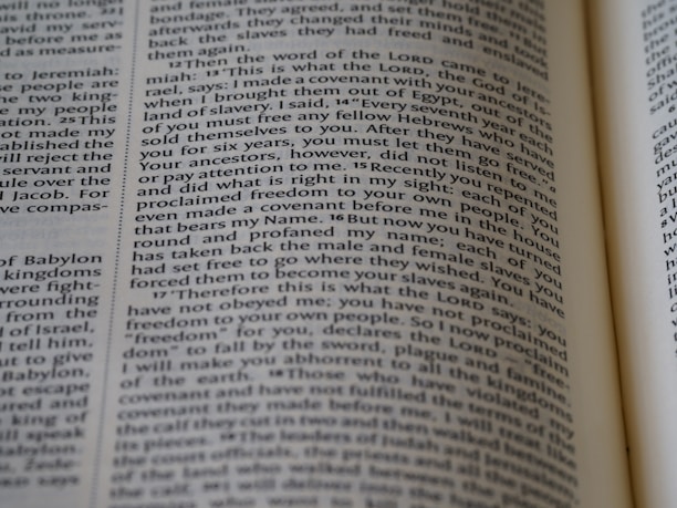 The image depicts an open book with text on its pages. The text is printed in a clear, serif font, oriented in columns. The visible content includes religious or biblical references and structured paragraphs. There is a focus on the words, which are highlighted by the close-up shot.