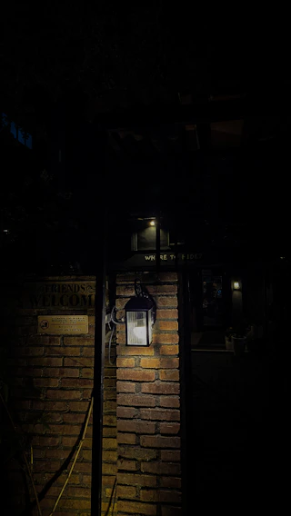 A weathered lantern casting flickering light over an old wooden sign that reads 'Welcome to The Hollow' at twilight.