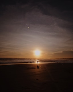 Sunrise silhouette of a lone runner on a beach with waves in the background.