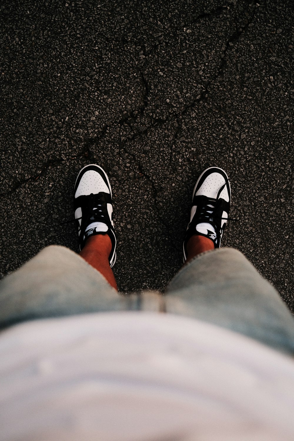 a person with black and white shoes standing on asphalt