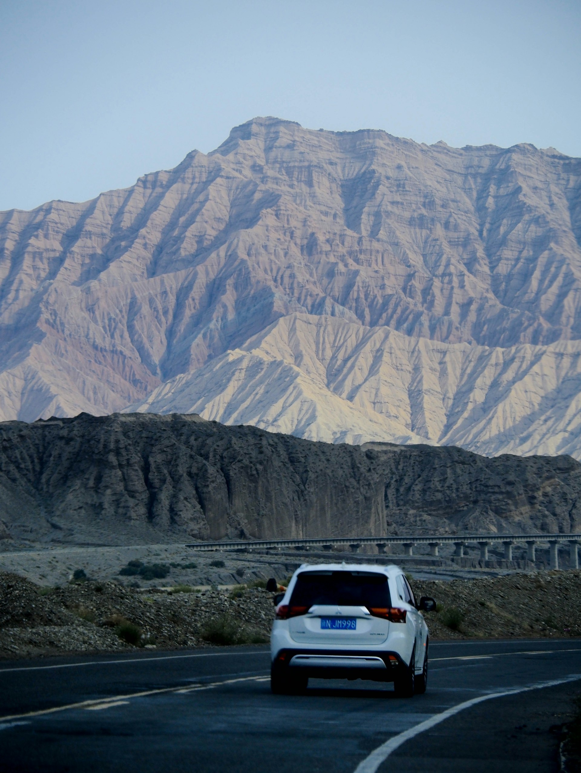 A vibrant red SUV cruising along a winding mountain road under a clear blue sky.