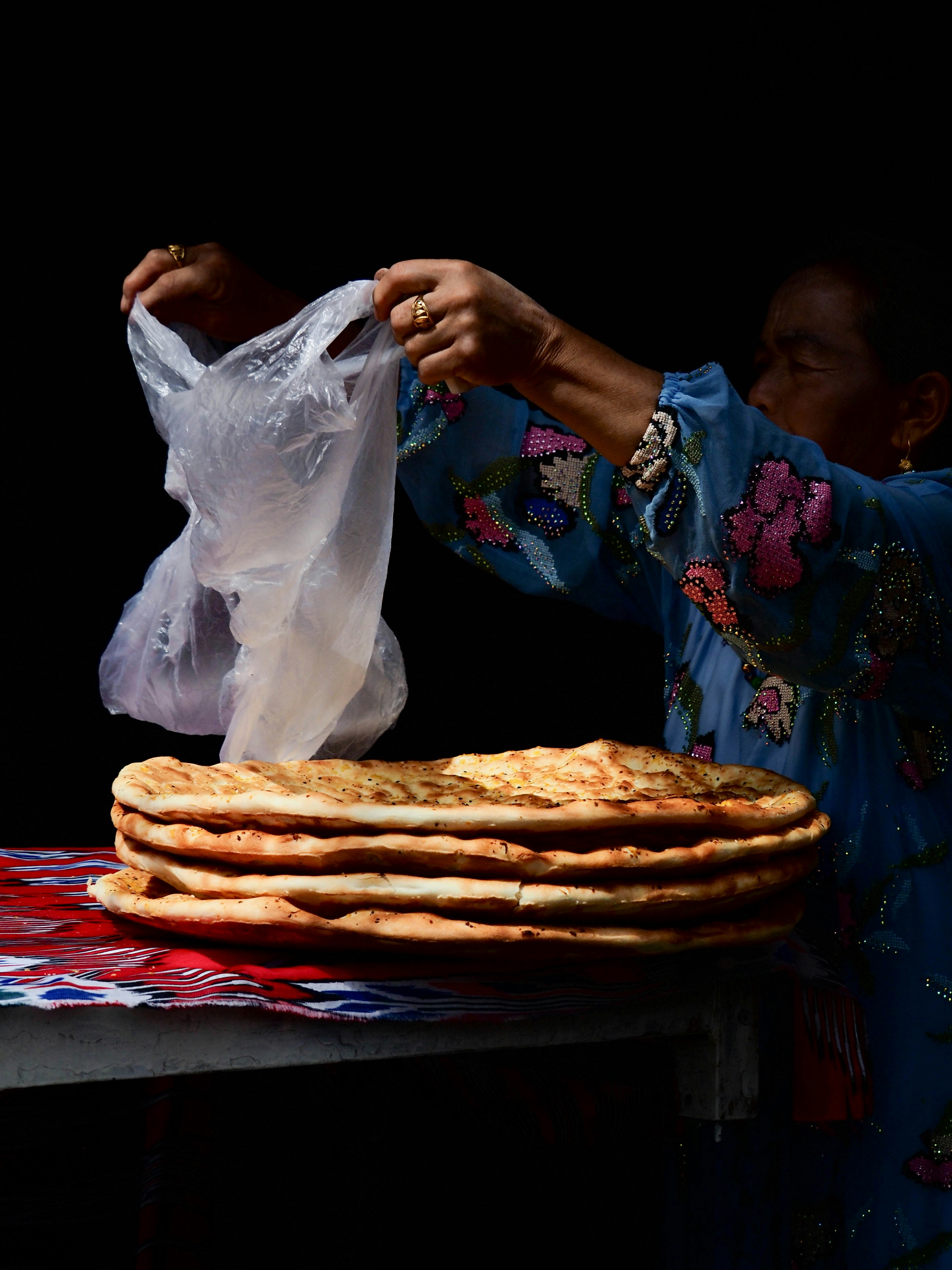 a woman holding a plastic bag over a stack of flat bread