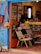 A cozy, eclectic shop interior featuring a mix of colorful, decorative textiles and furniture. The blue, open door invites you into a warm space filled with patterned rugs and chairs draped in textile designs. On the wall, bags hang as decorations alongside other woven art pieces. A counter at the back is partially visible, holding various items and a plant, contributing to a welcoming, artistic atmosphere.