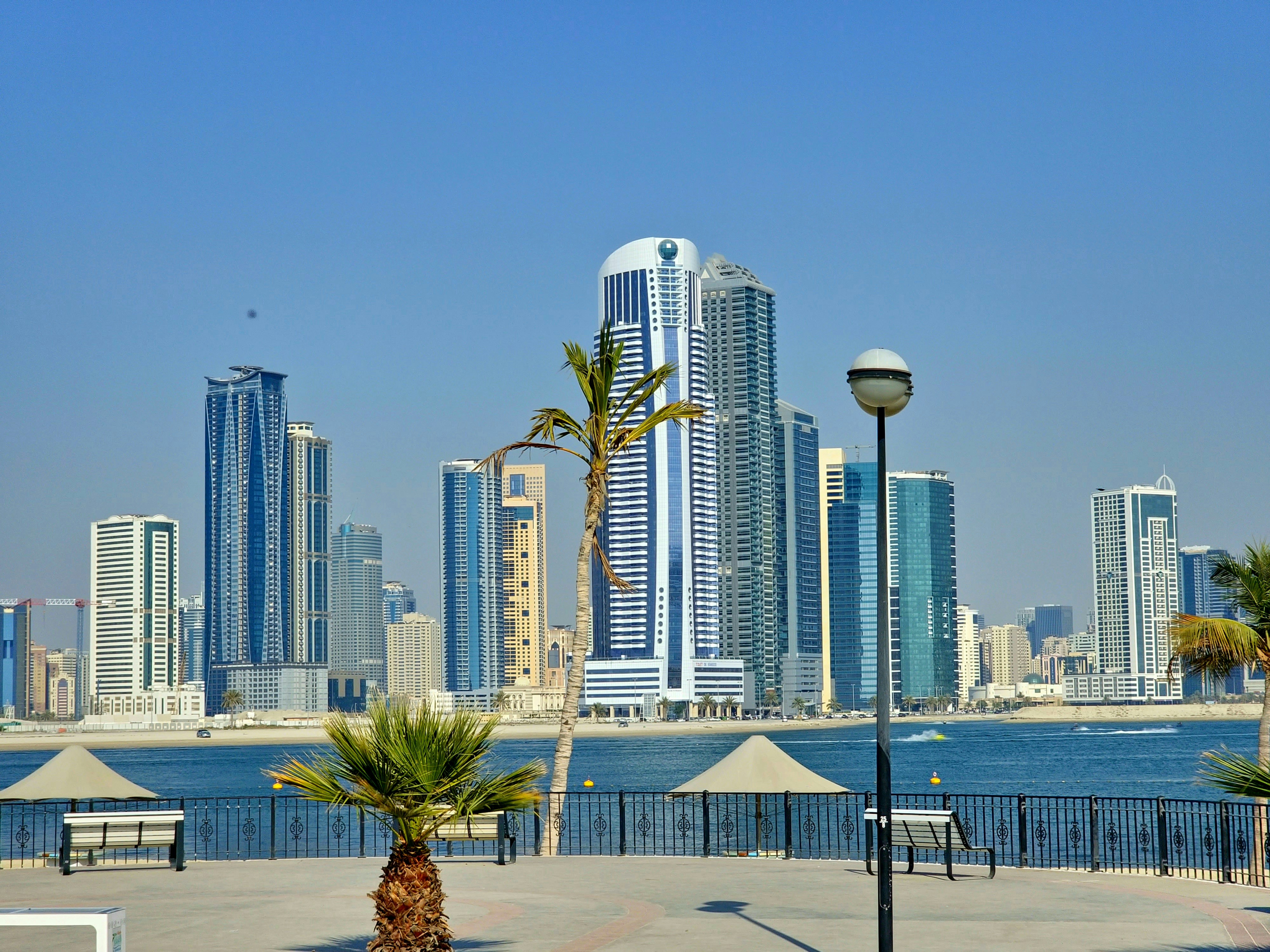 Al Reem Island modern skyline from across the water, bright daytime, blue sky, gleaming towers, well-lit open waterfront