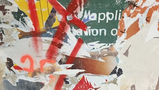 A collage of torn and overlapping posters with partially visible text and various layers of paper. Bold splashes of red paint and vibrant colors like green, yellow, and orange intersect with the ripped textures.