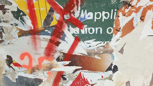 A collage of torn and overlapping posters with partially visible text and various layers of paper. Bold splashes of red paint and vibrant colors like green, yellow, and orange intersect with the ripped textures.