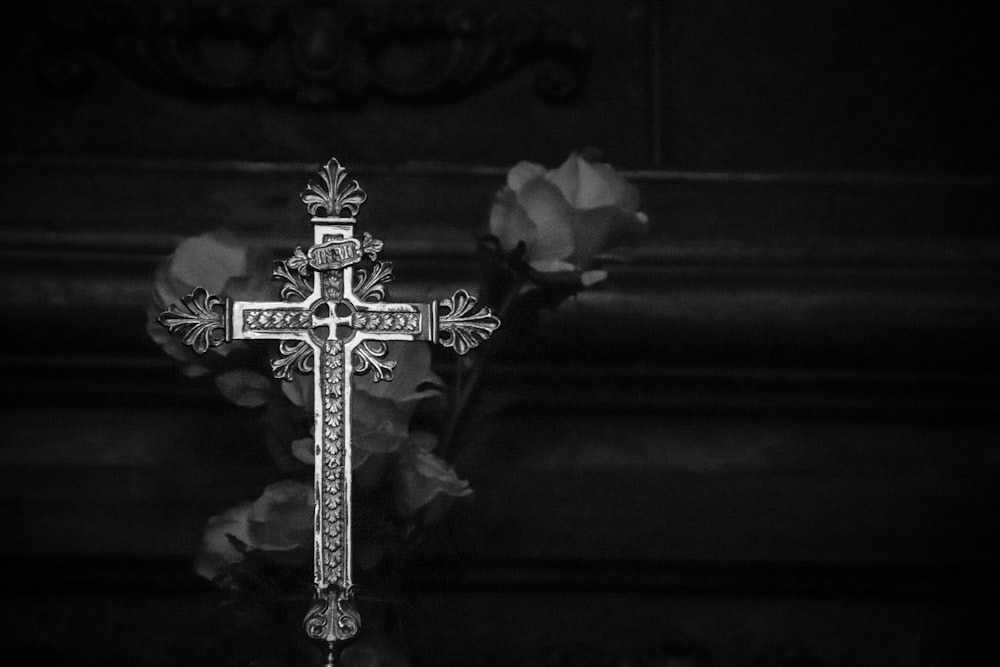 a black and white photo of a cross and flowers