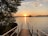 Sunset view over a serene lake with a small dock and lush greenery.