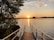 Sunset view over a serene lake with a small dock and lush greenery.