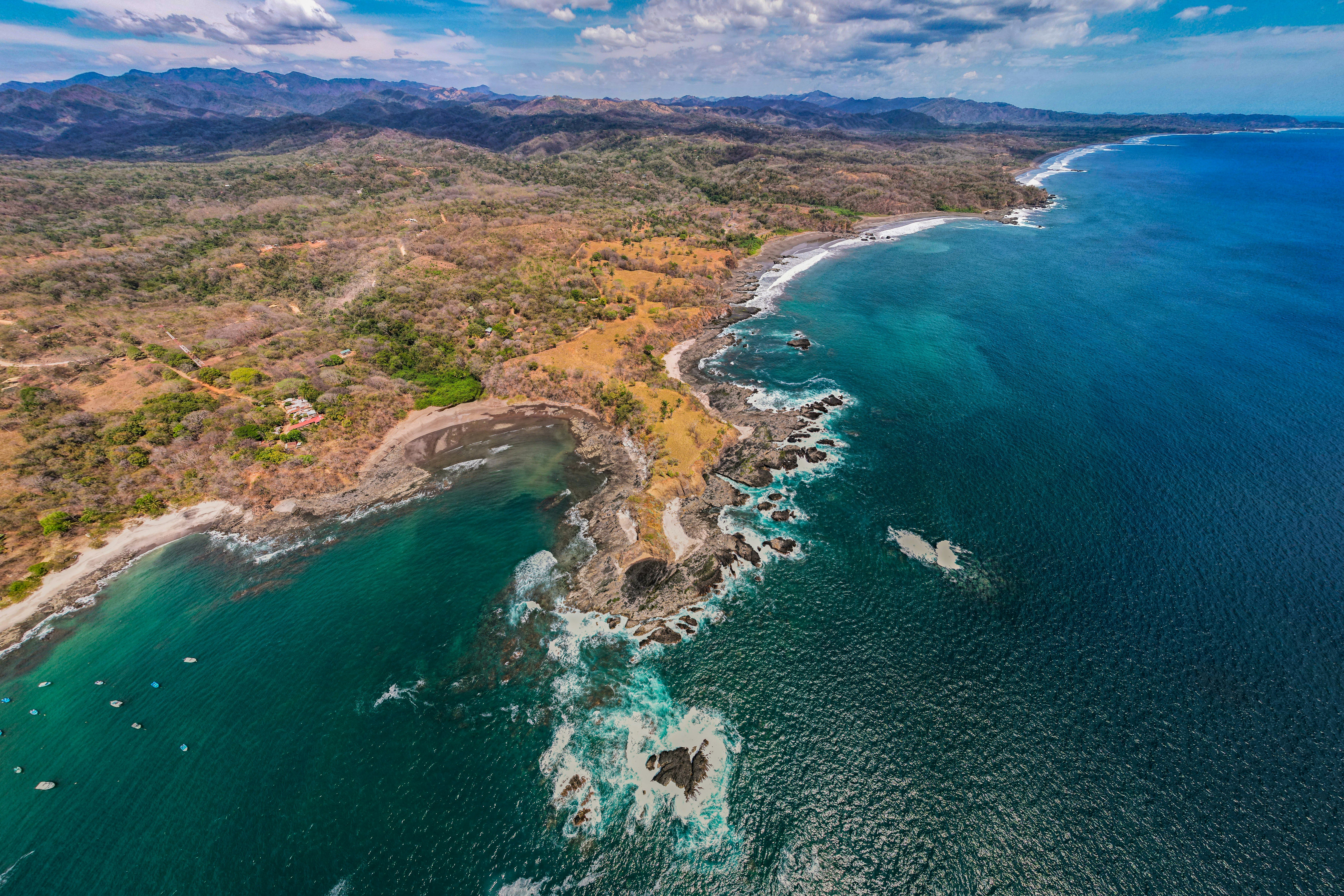 Stunning aerial view of Costa del Sol coastline with turquoise Mediterranean sea, golden sandy beach, and green hillside, bright sunny day