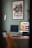 A modern workspace featuring a desktop computer, laptop on a stand, and a tablet on a wooden desk. A framed art poster titled 'The Grand Tour' is displayed on the wall. A sleek desk lamp provides additional lighting. Books and a small speaker are also present, contributing to the aesthetic setup.