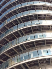 Several curved balconies with glass railings are stacked in a pattern on a high-rise building. The structure features a repetitive architectural design, emphasizing the symmetry and modern materials.