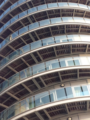 Several curved balconies with glass railings are stacked in a pattern on a high-rise building. The structure features a repetitive architectural design, emphasizing the symmetry and modern materials.