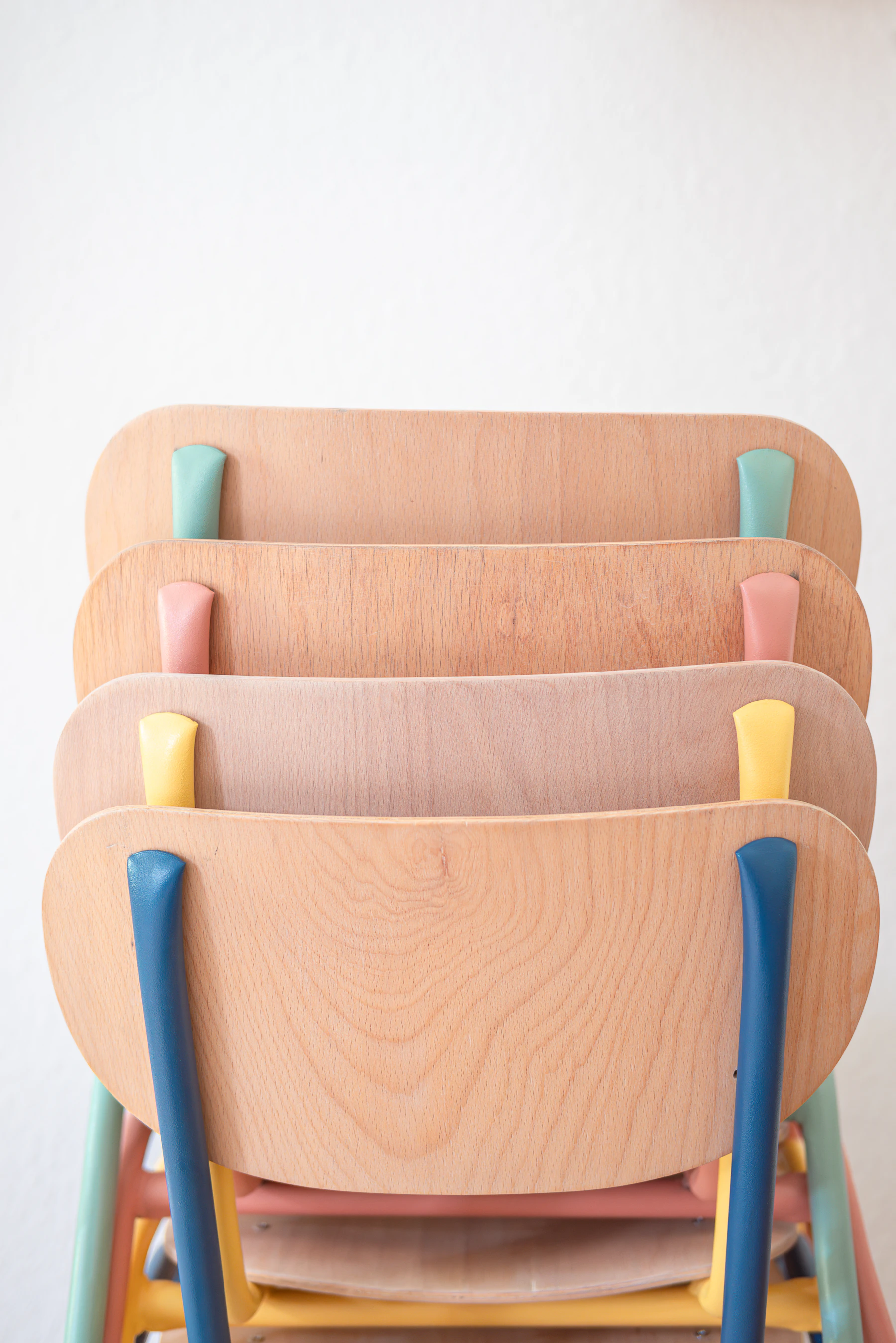 A stack of small plywood chairs with pastel-painted legs, blue, pink, yellow, mint