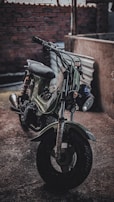 An artistic photo of a vintage motorcycle parked against a dark industrial backdrop.