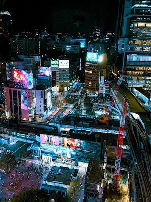 Nighttime cityscape featuring illuminated outdoor LED displays along busy streets near train stations.