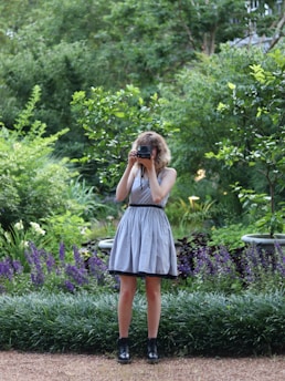 Photo of a woman holding gardening tools, standing in a lush garden.