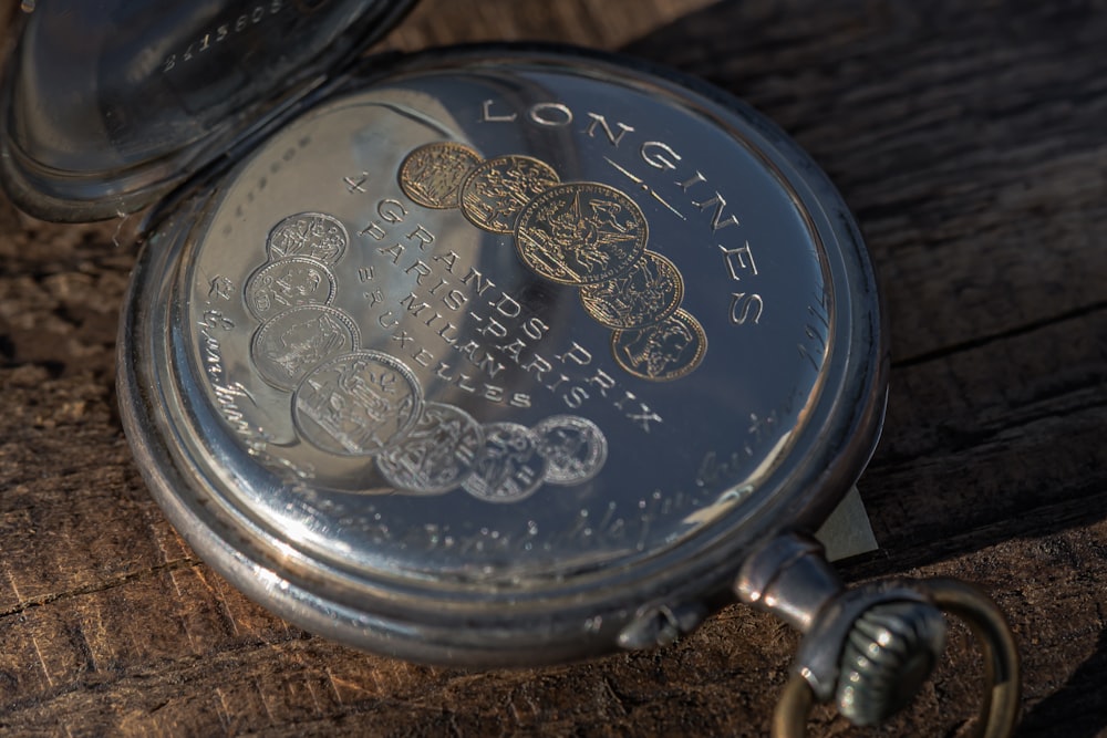 a silver pocket watch sitting on top of a wooden table