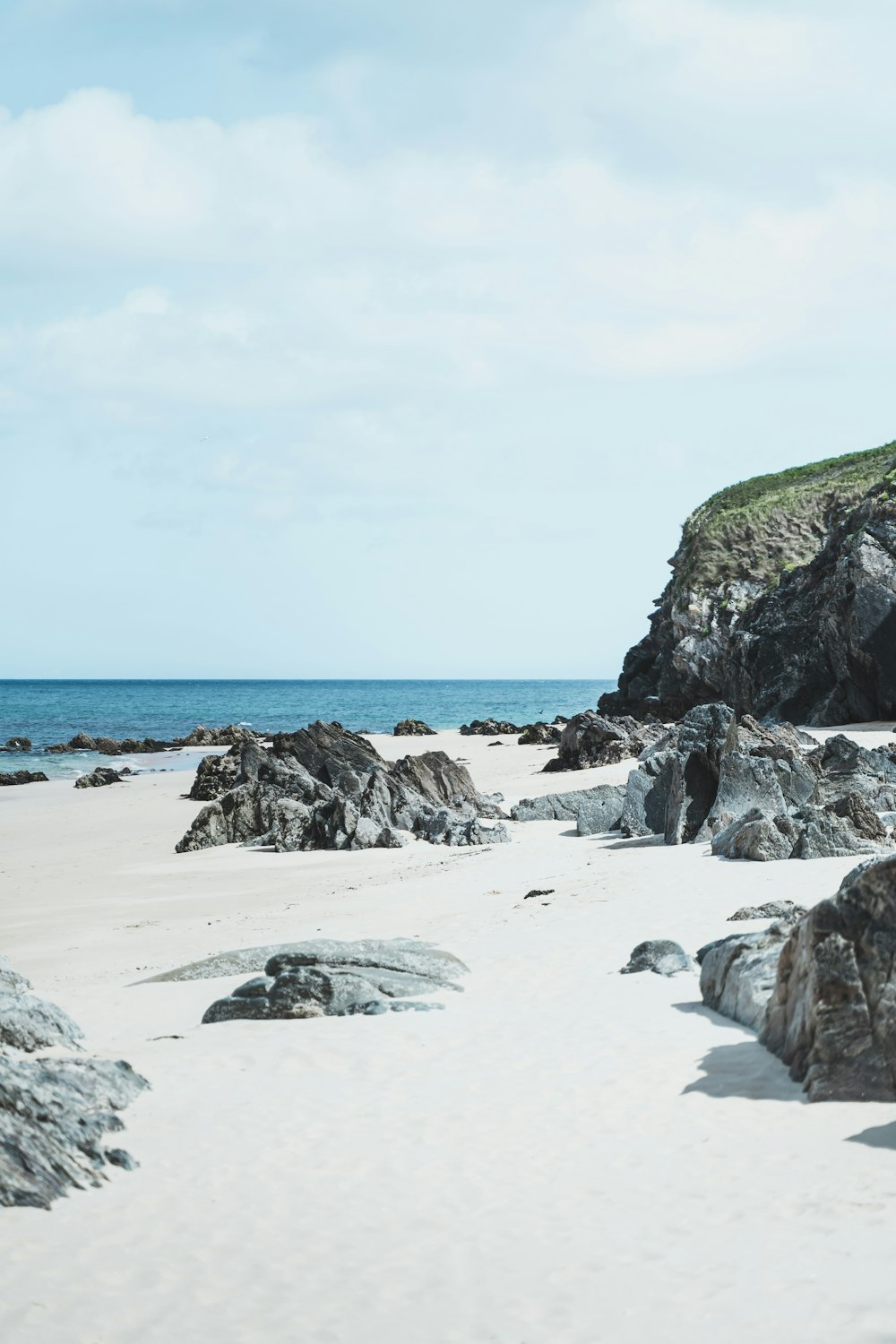 a sandy beach with rocks and a hill in the background