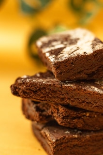 A close-up of a rich, fudgy chocolate brownie with a glossy top and a sprinkle of powdered sugar.