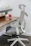 A modern ergonomic office chair with a gray cushioning sits beside a wooden desk. On the desk, there is a red coffee mug and a red notebook. A small potted plant adds a touch of nature to the workspace.