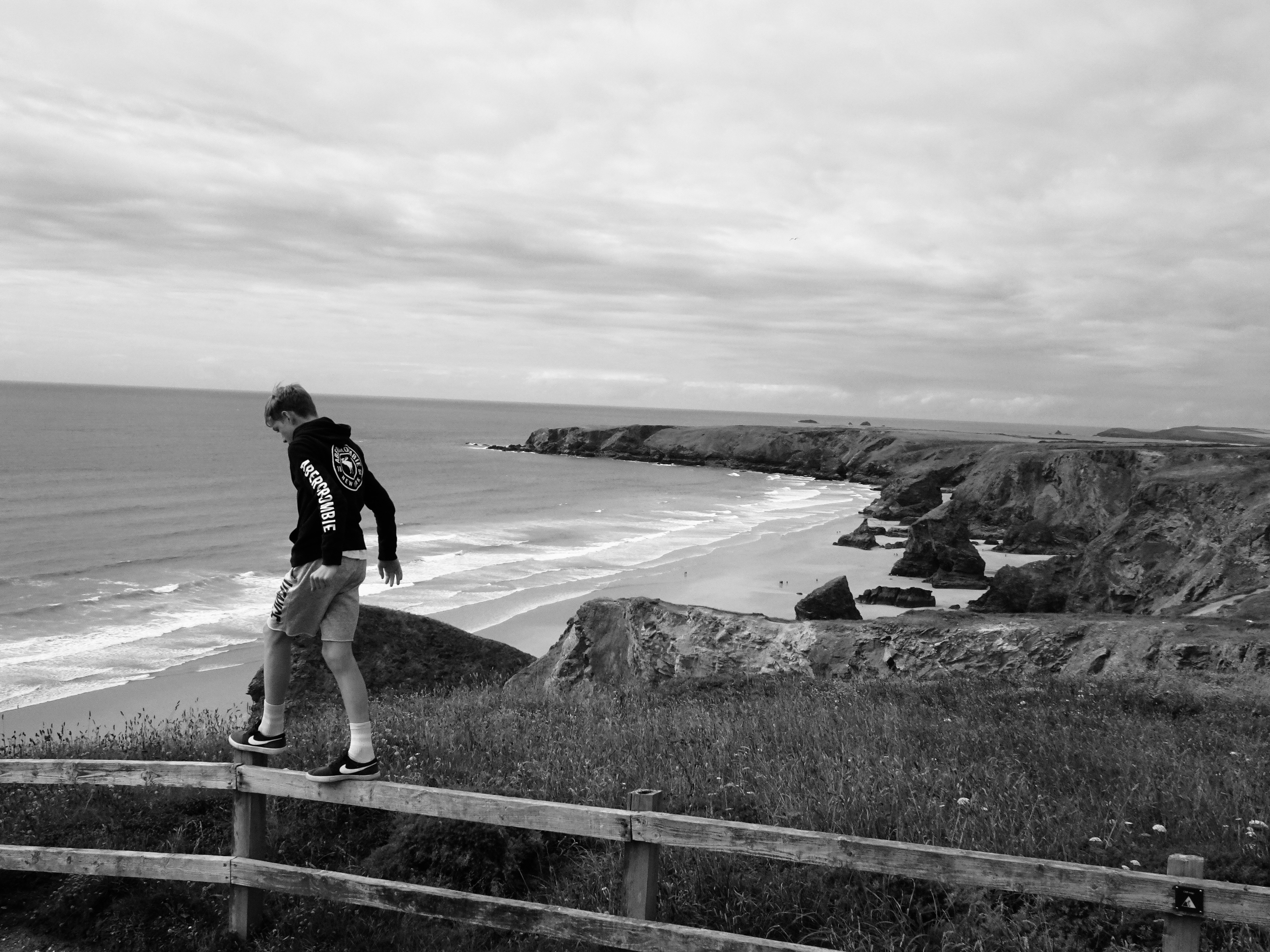 a man standing on top of a wooden fence next to the ocean