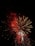 A vibrant display of fireworks with bright red and white bursts, set against the dark night sky. The fireworks are exploding in various shapes and sizes, creating a dazzling spectacle.
