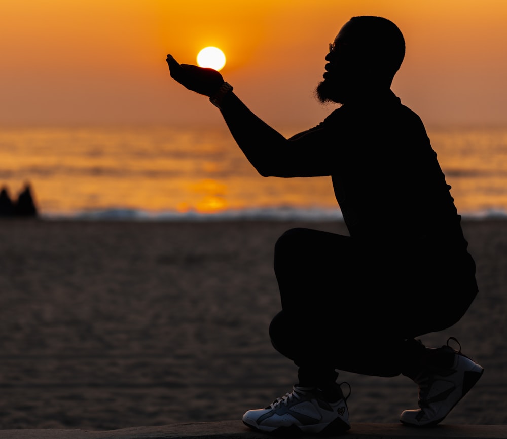 a silhouette of a man sitting on a beach at sunset