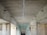 A symmetrical view under a concrete bridge, showing the ceiling with longitudinal lines and multiple surveillance cameras mounted on either side. The perspective converges towards the center, creating a tunnel-like effect. Natural light illuminates the structure's textured surfaces and angular shapes.