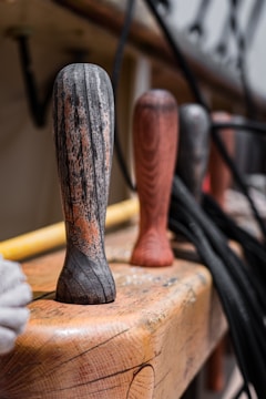 Wooden handles with a weathered texture lined up on a wooden surface, accompanied by coiled black ropes and hardware components in a blurred background.