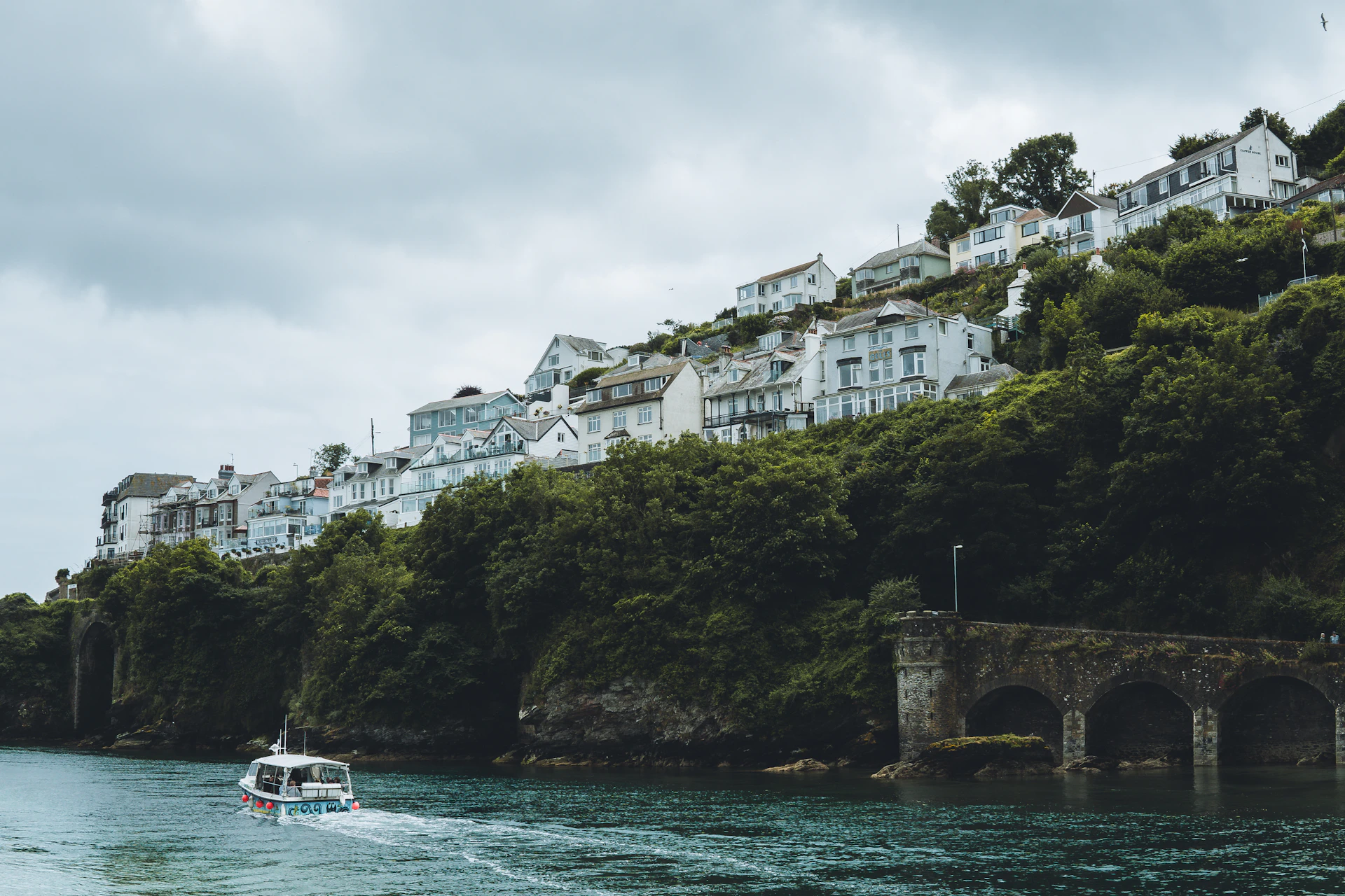 A boat going down a Cornish river between green, wooded banks