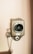 A vintage wall-mounted telephone with a wooden casing and a large central speaker. It features a metal earpiece connected by a cord and intricate metal fittings. The background is a plain light-colored wall.