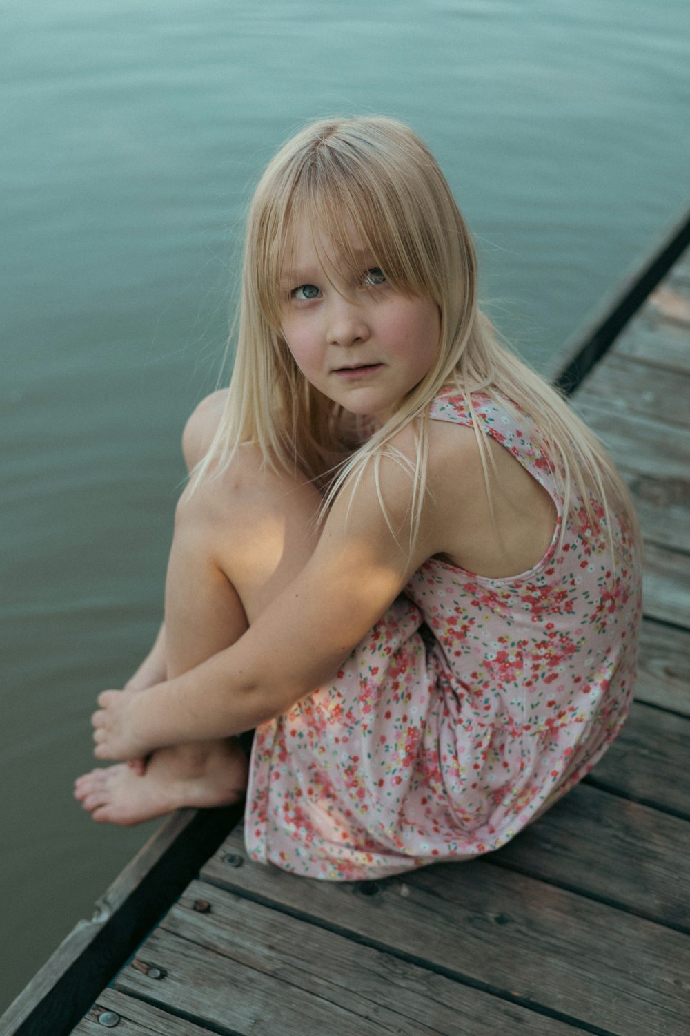 a little girl sitting on a dock by the water