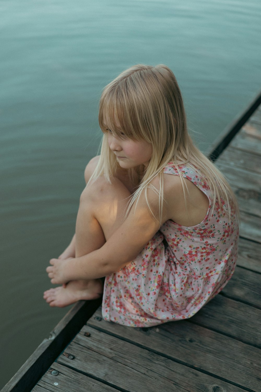 a little girl sitting on a dock by the water