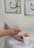 A person is using a spatula to scoop a pink gel-like substance from a container labeled 'Maria Galland Paris'. The person is wearing a white shirt, and the background includes abstract artwork and a white table.
