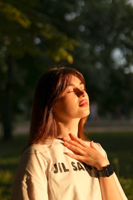 a woman standing in a park with her hands on her chest