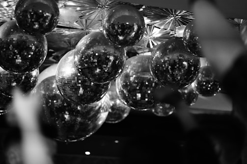 A collection of disco balls hangs from the ceiling, reflecting light in a multitude of directions. The intricate patterns on the ceiling complement the mirrored surfaces of the disco balls, creating a dynamic and festive atmosphere.