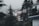 A foggy residential area with multiple houses surrounded by tall evergreen trees. The houses are mostly wooden with some white siding, and one has a small elevated deck. The fog adds a misty atmosphere to the scene.