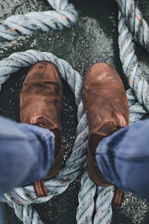 A pair of brown leather boots standing on top of thick, coiled ropes with a textured surface beneath.
