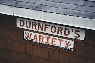 The image features a weathered sign on a wooden structure with the words 'DURNFORD'S VARIETY' in bold red letters against a white background. The roof is covered in dark gray shingles.
